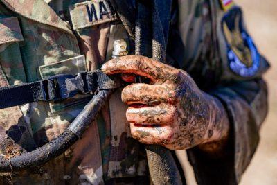  Close-up of a cadet’s arm and hand covered in mud from Platoon Tactical Challenge. The cadet’s uniform and straps are also muddy.